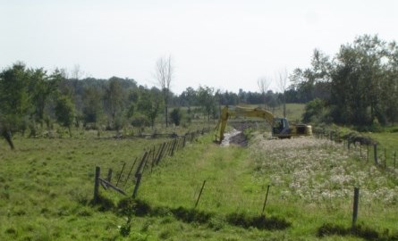 backhoe creating a ditch in a field